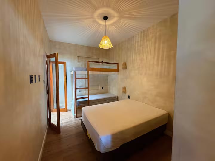 Quarto da Casa Tohmé com cama de casal, beliche ao fundo e acabamento em cimento queimado.