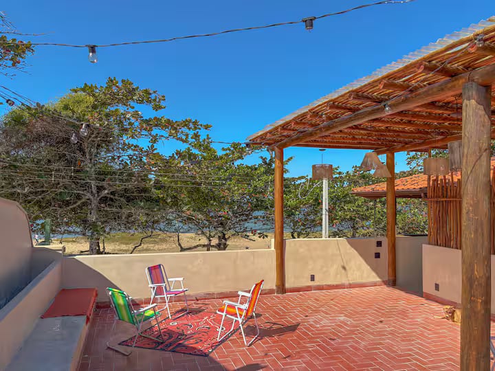 Rooftop da Casa Tohmé com pergolado de madeira, cadeiras de praia e a praia ao fundo.